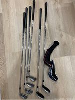 All golf clubs laid out on floor showing grip ends and club heads along with two hybrid head covers.