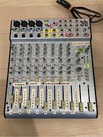 Top-down view of the Alesis Multimix 12 FXd audio mixer showing input jacks, knobs, faders, and LED indicators with labels on faders.