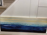 Photo showing the full length of the calm ocean acrylic canvas painting leaning against white wall and staircase.
