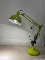 Green adjustable table lamp lit, showing dome-shaped shade and round base on floor.