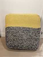 Front view of square floor pillow with yellow knitted top half and black-and-white marled lower half.