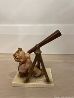 Side angle showing the boy figurine looking through the telescope on a tripod, base with M.J. Hummel signature visible.