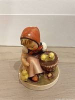 Front view of Hummel figurine showing girl feeding chicks in basket and one chick outside.