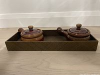 Two brown ceramic onion soup pots with lids and handles in a rectangular tray, shown side view.