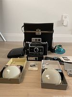 Complete lot overview showing Polaroid camera, carrying case, film holders, manuals, and small accessories arranged on floor.