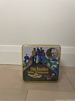 Front of the Beatles Yellow Submarine album cover tin with colorful illustration of the band and text.