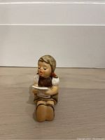 Front view of vintage Hummel figurine of a seated girl reading a book, showing face and front details.