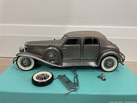 Side view of the Franklin Mint 1933 Duesenberg model car with one wheel removed and front grille and hood ornament detached beside it.