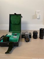 Overview of camera body with attached lens, two additional lenses, and green velvet lined black carrying case