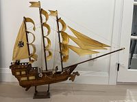 Side view of wooden model ship showing three masts with yellow sails and black crosses, displayed on a wooden base.