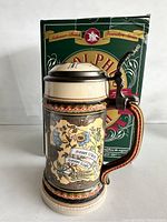 Adolphus Busch beer stein front view showing full colorful artwork and handle, standing next to original box with founder's image and text.