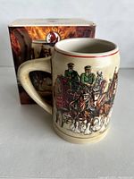 Front view of cream-colored ceramic mug with detailed colored illustration of Budweiser Clydesdale horses pulling a wagon, with original box in background.
