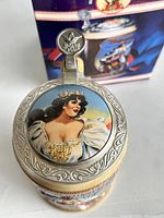 Close-up photo of the beer stein lid showing the colorful depiction of a woman and embossed metal lid with Budweiser eagle emblem.
