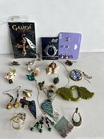 Overview of entire jewelry lot showing multiple earrings, pendants, and the Gaudi cross in packaging