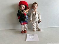 Two Norman Rockwell dolls displayed side by side on a white background including the red-capped Mimi doll holding a baby doll and the Davey doll with stethoscope in pajamas.