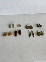 Lot of 8 pairs of assorted earrings including Scrabble tile earrings, green rectangular earrings, grape cluster earrings, and round multi-layered disc earrings