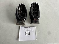Front view of two black ceramic Hamsa hand figurines, each shaped like a left hand and standing upright.