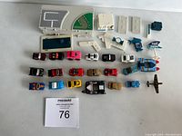 Full display of approximately 22 vintage toy cars along with various accessory pieces including miniature buildings and street layout pieces.