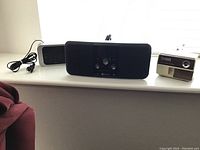 View of the three main items on a windowsill: Boston Bluetooth speaker dock center, Timex digital alarm clock left side, Panasonic electric pencil sharpener right side.