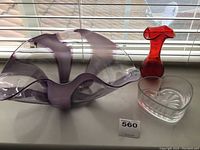 Front view of large purple bowl, red vase, and heart-shaped clear candy dish on window ledge