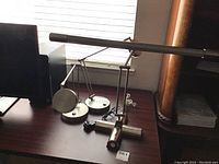 Set of three desk lamps on a dark wood desk; two metal and one plastic looking like metal; adjustable arms and round heads; cords visible