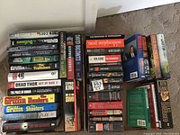 Books stacked in three piles showing titles and authors including multiple books by Griffin and Baldacci, Brad Thor, and others.