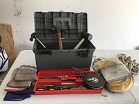 Photo showing an open gray plastic toolbox with hammers and mallet inside, red tool tray with hand tools, gloves to the left, coiled rope, and yellow extension cords on the right.