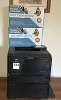 Black HP LaserJet Pro 400 printer with two boxes of premium compatible laser toner cartridges stacked on top