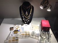 Jewelry display bust with necklaces, small organizers with jewelry findings, earrings, and red jewelry boxes with tools nearby