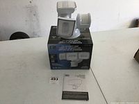 Photo of LED security light on top of its box with instruction manual in front showing new condition.