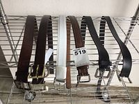 Five men's belts displayed on a metal rack, showing different colors and buckle styles.