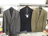 Three men's dress jackets hanging on a metal rack: gray, black, and light brown checked patterns.