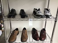 Four pairs of men's shoes displayed on metal shelves: black leather dress shoes, gray and black Nike sneakers, tan suede casual shoes, and brown leather dress shoes.