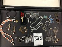 Overview of assorted novelty jewelry including necklaces, earrings, brooches, and keychains in a case