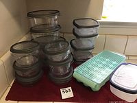 Clear round plastic storage containers with gray lids stacked in two piles, next to a light blue egg container with lid.