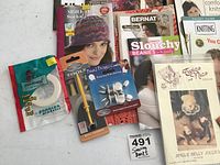 Close-up of various sewing and knitting books, craft packs including bead bug pack and floral tape, and assorted notions with knitting patterns visible.