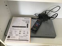 Panasonic Blu-ray disc player with remote and user manual on top, power cables coiled beside it.