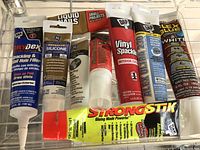 Photo of various small project glues and sealants arranged in a tray, showing tube labels and packaging.