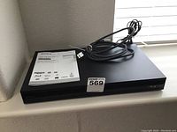 Top and front view of black Sony DVD player with HDMI cable and user manual on top