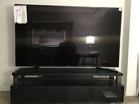 Front view of flat-screen TV sitting on black wood laminate stand with window reflection visible