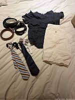Full view of navy blue t-shirt with white dots, white shorts, two neckties, and three belts on white bedspread.