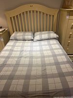 Full view of assembled double bed frame with plaid bedding showing the headboard and part of the footboard and surrounding furniture.