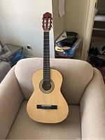 Full view of the Guvnor classical acoustic guitar sitting on a beige armchair, showing the entire body and neck.