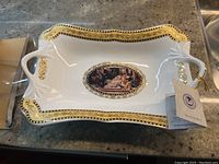 Porcelain dish rectangular with dual handles, decorated with gold and black ornate border and classical art image at center.