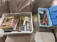 Wide shot showing two plastic containers filled with kids art supplies on a beige couch.