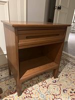 Side angle showing the full night table with drawer closed and open lower space, resting on a patterned carpet.