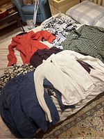 Seven men's medium shirts laid out on beds and a chair, showing various colors and patterns including floral, checkered, and solid colors.
