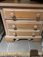 Front view of wooden night table showing 3 drawers with round wooden knobs and decorative molding on the lower edge.