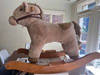 Side view of the plush rocking horse, showing the full body covered in soft beige and brown fabric with wooden rocker base.