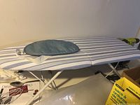 Photo of the tabletop folding ironing board showing striped fabric cover and ironing glove placed on top.